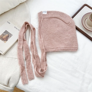 Detailed close-up of pink knit ear-flap hat with ties on soft fabric background