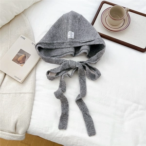 Grey knit hooded bonnet with long ties on a cozy white bedsheet for winter fashion