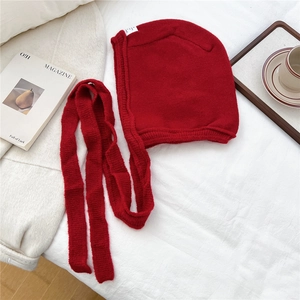 Detailed texture of a bright red knitted hood hat with long drawstring ties on white fabric