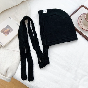 Close-up of black chunky knit hooded scarf with ties on white cozy bedding background