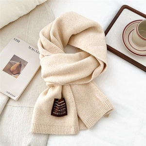 Close-up of beige knit scarf texture with handmade label on soft cotton background