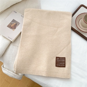 Detail of cream knitted scarf showing the wool handmade leather tag on soft fabric