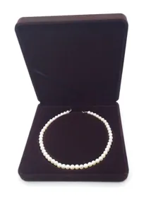Macro shot of single-strand white pearl necklace inside a brown velvet jewelry gift box