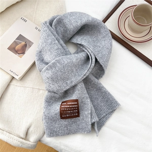 Close-up of grey wool knit scarf texture with a handmade leather label on white fabric