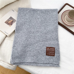 Close-up of light grey knit scarf texture with handmade brown leather label detail