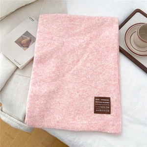 Detail of pink knitted scarf with brown leather tag and care icons on soft white bedding