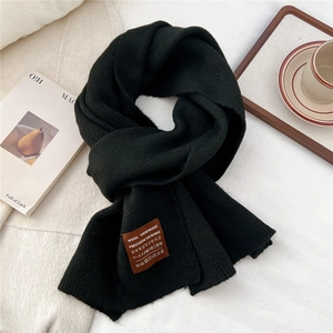 Detail of black knitted scarf with premium leather label on a cozy winter backdrop