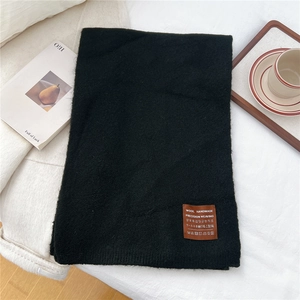 Detailed close-up of thick black knitted scarf fabric texture and brown leather label
