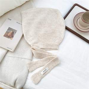 Detail of cream knit bonnet showing vertical ribbed texture and logo label on long ties
