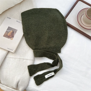 Close-up of dark green knitted hooded scarf with branded logo label on soft white background