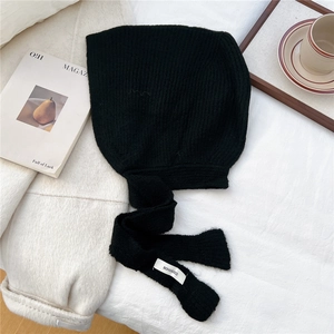 Detail of black rib-knit balaclava with logo label on long ties and warm wool texture