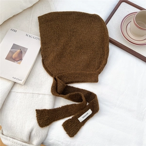 Detail of dark brown knitted bonnet with earflaps and brand label on soft fabric