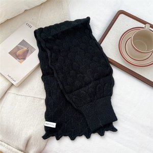 Detail of black knit scarf featuring a raised scale texture and ribbed scalloped edges