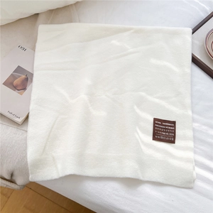 Détail macro d'une écharpe en laine blanche avec étiquette en cuir cousue main sur tissu
