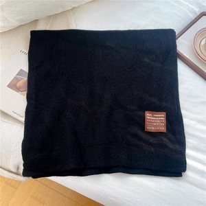 Détail de l'écharpe en laine noire faite à la main avec étiquette en cuir sur le lit