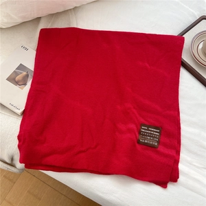 Détail d'une écharpe en laine rouge avec étiquette artisanale sur fond de tissu blanc