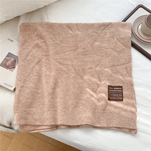 Détail d'une écharpe en maille avoine avec texture laine et patch cuir sur lit blanc