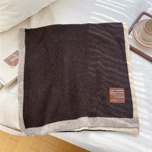 Detail of wool knit scarf with handmade label and contrast color border on white bed