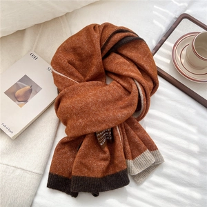 Close-up of caramel knit scarf with color-block detail and fabric care label on white bed
