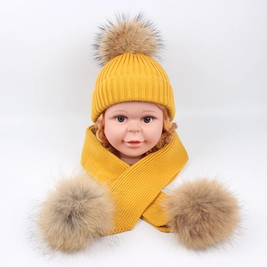 Detail of yellow knit baby hat and scarf set featuring large fluffy faux fur pom-poms