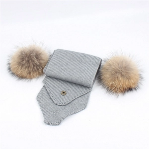 Detail of light gray chunky knit scarf featuring fluffy fur pom-poms and metal snap buttons