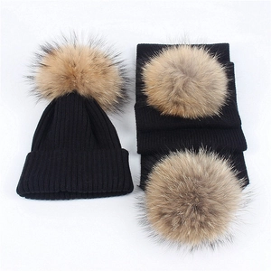 Flat lay detail of black ribbed knit winter set with fluffy faux fur pom-poms on white background