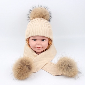 Beige knitted baby hat and scarf set with fluffy brown faux fur pom-poms for winter warmth