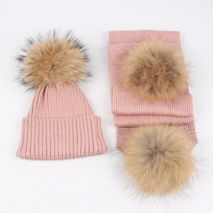 Detailed view of pink knitted baby hat and scarf set with large fluffy fur pom-poms