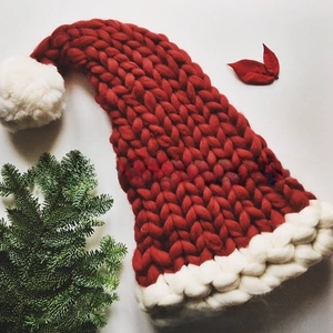 Detail of red and white thick chunky knit Christmas hat with fluffy pom-pom and pine accents