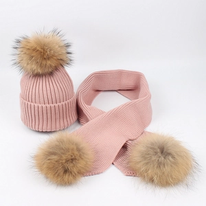 Close-up of pink ribbed knit hat and scarf set with fluffy brown fur pom-poms details
