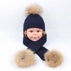 Detail of navy blue ribbed knit hat and scarf set with thick tan faux fur pom-poms