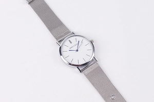 Close-up of minimalist silver quartz watch with white dial and blue hands on mesh strap