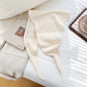 Detail of cream white knitted triangle scarf with delicate openwork pattern on white bedding
