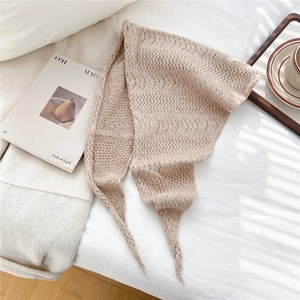 Close-up of beige knit neckerchief with hollow crochet pattern on soft fabric