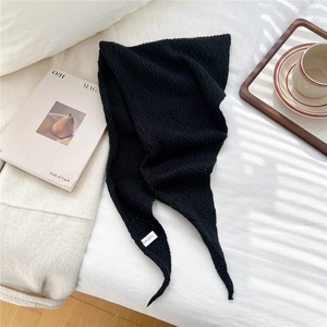 Close-up of black chunky knit triangular scarf with a soft texture and woven label