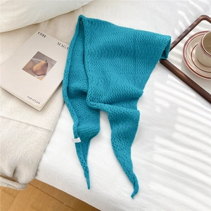 Detailed close-up of blue knit scarf with hollow crochet texture on white bedsheet