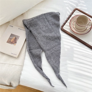 Close-up of gray knit triangle scarf with delicate hollow lace pattern on white bedding
