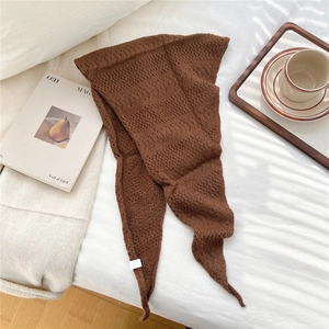 Close-up of dark brown knit triangle scarf with textured grainy pattern on a bed