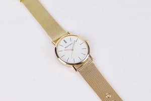 Detail shot of a minimalist gold mesh watch with a white dial and bar indices