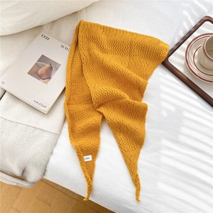 Detail of yellow knit triangle scarf showing soft texture and fabric label on white bedding