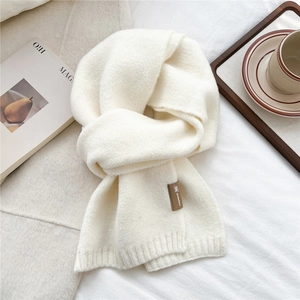 Detail of soft cream knitted scarf featuring a premium brown leather brand logo label