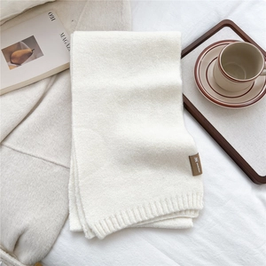 Detail view of cream knit scarf with textured ribbing and premium leather brand tag