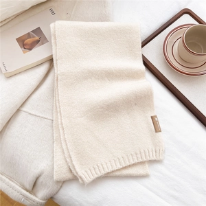 Close-up of cream knitted scarf with ribbed edge and leather tag on aesthetic background