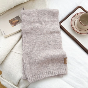 Detail of soft knitted scarf in dusty rose with a stylish leather logo label on textured fabric