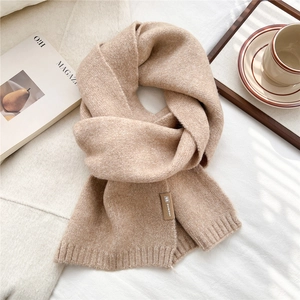 Macro view of beige chunky knit scarf texture with leather tag on soft white bedding