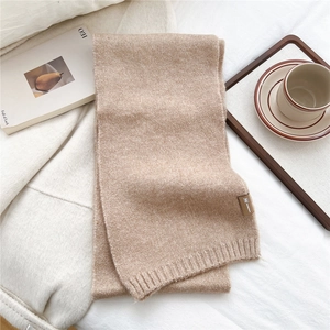 Detail of soft beige knitted scarf texture with a brown leather tag on a cozy tray