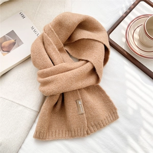 Detail of camel knit scarf with ribbed edges and brand label on a cozy winter backdrop