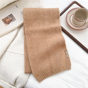 Close-up of camel knitted scarf featuring a woven label on soft textured fabric