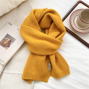 Detailed close-up of a warm yellow knitted scarf featuring a brown leather brand tag