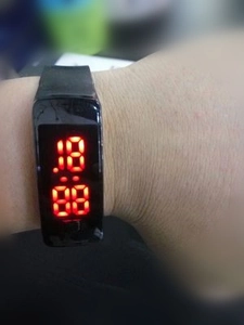 Wrist view of a black LED digital sports bracelet with red display showing time